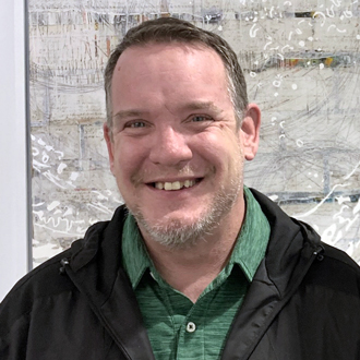 Jerry smiling, facing forward, short hair and beard, black jacket, green shirt