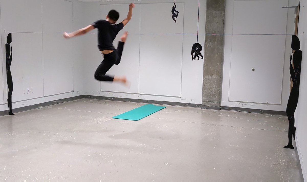 Jeremy dancing in mid-air in a white room with a small bright blue mat on the floor.