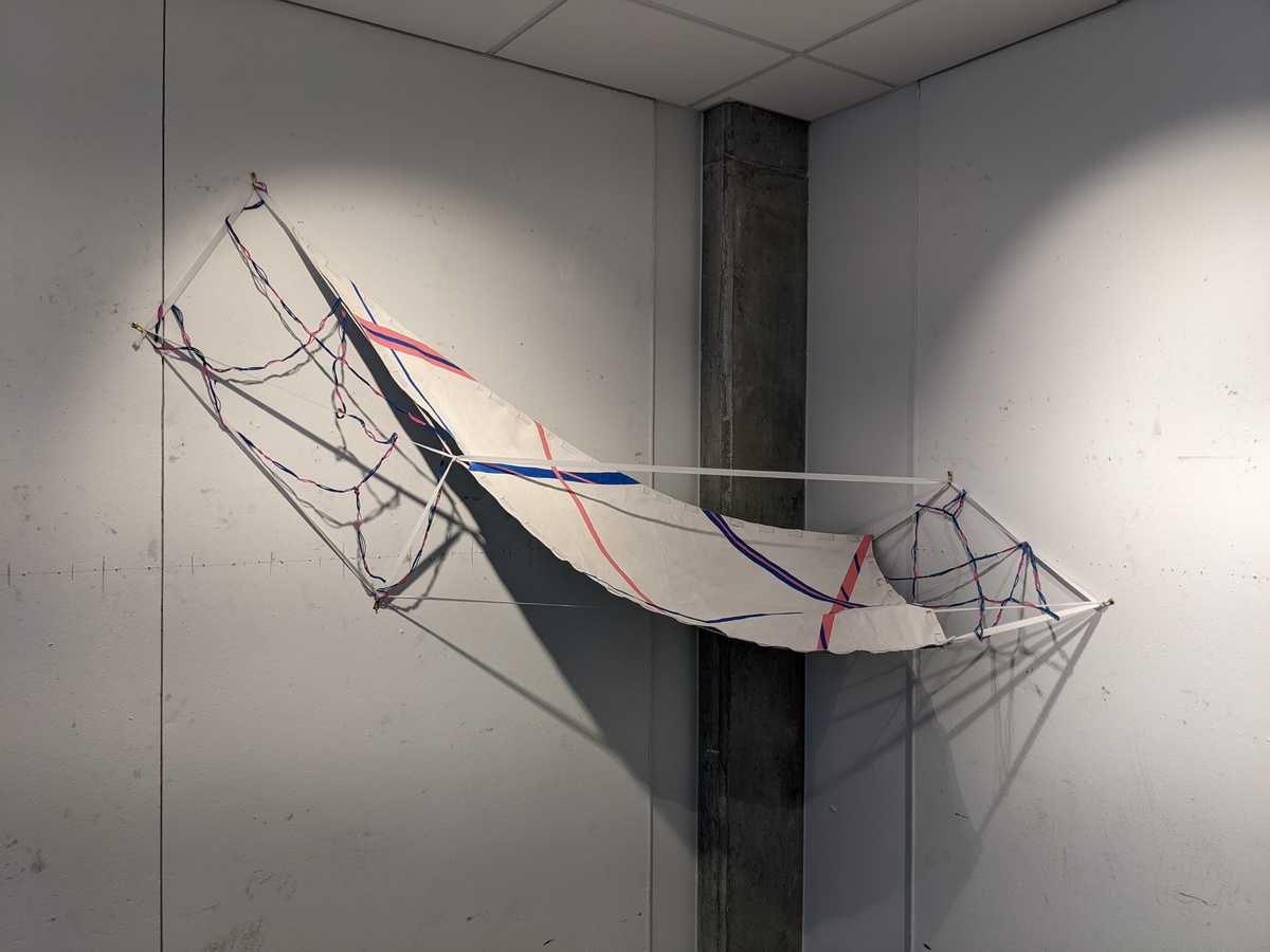 A sculptural object that resembles a hammock draped across the corner of a room.