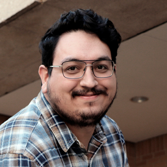 Kevin Contreras facing forward, smiling, wearing glasses, beard and mustache, plaid shirt