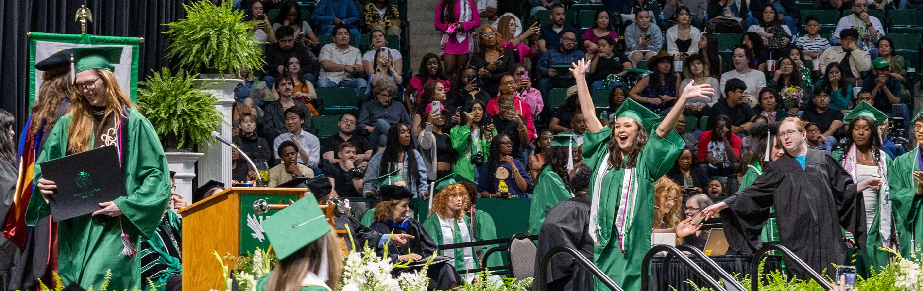 Student on stage throws her arms up in celebration.