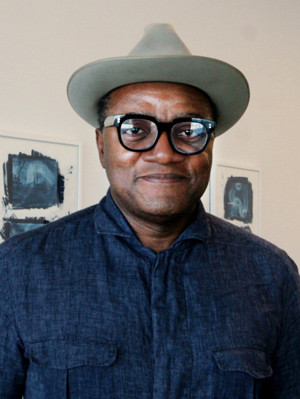 Christopher Blay, wearing glasses, a fedora, dark blue shirt, smiling