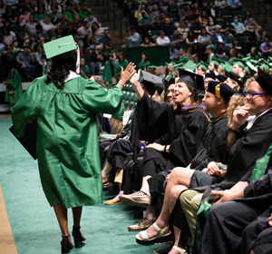 Graduate in academic regalia gets a high-five from a faculty member at a Commencement Ceremony.