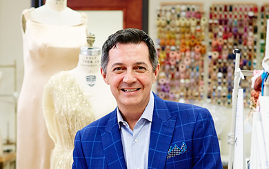 Michael Faircloth is smiling and facing forward. He wears a blue jacket over a shirt. Mannequins and thread are in the background,