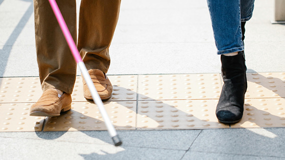 The lower legs and shoes are shown with one person using a white cane for the blind.