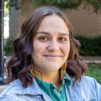 Jennifer is facing forward and smiling. She has brown wavy hair and wears a blue shirt.