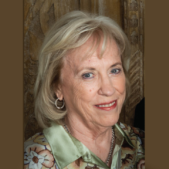 Susan is facing forward and smiling. She has blonde hair and wears a green print blouse.