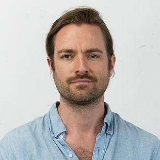 Brian facing forward, brown hair, mustache and beard; he is wearing a blue shirt.