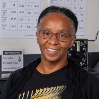 Letitia is facing forward and smiling. Her hair is pulled back and she wears a black t-shirt.