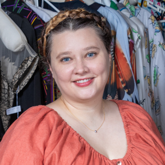 Pankonien is facing forward and smiling. Her hair is up in a braid, she wears a necklace and an orange blouse.