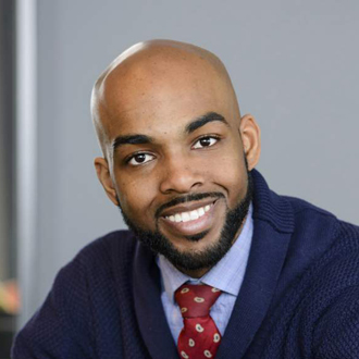 Omari is facing forward and smiling. He has a bald head, dark mustache and a beard and wears a marroon tie with a dark blue jacket and shirt.