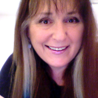 Ruth is facing forward and smiling. She has long brown hair and wears a black top.