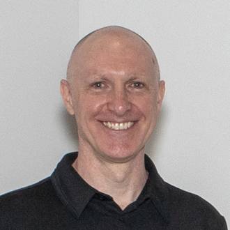 David is facing forward and smiling. He is bald and wears a black shirt.