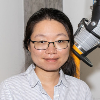 Donny is facing forward and smiling. Her dark hair is pulled back, she wears glasses and a white shirt.