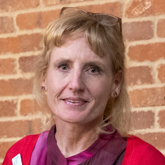 Elaine is facing forward smiling. She has light brown hair and wears a red top.