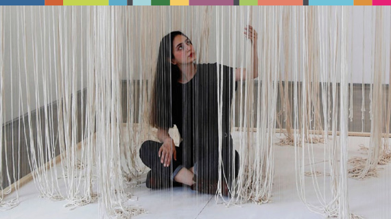 Woman sitting on the floor among ropes dangling from above.