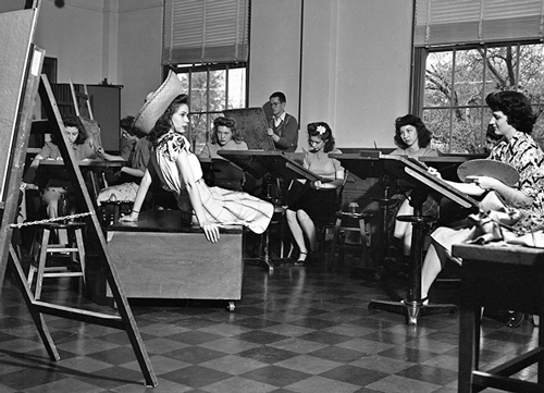 1942 photo of student sketching a live model posing in the center of the room.