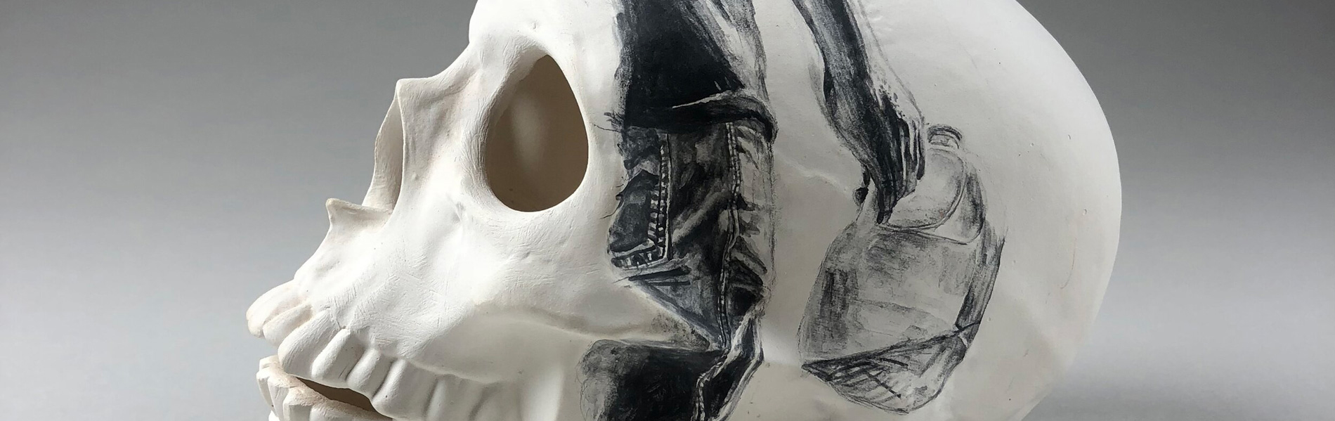 Detail of a white ceramic skull with a drawing on it of a person carrying a plastic water jug