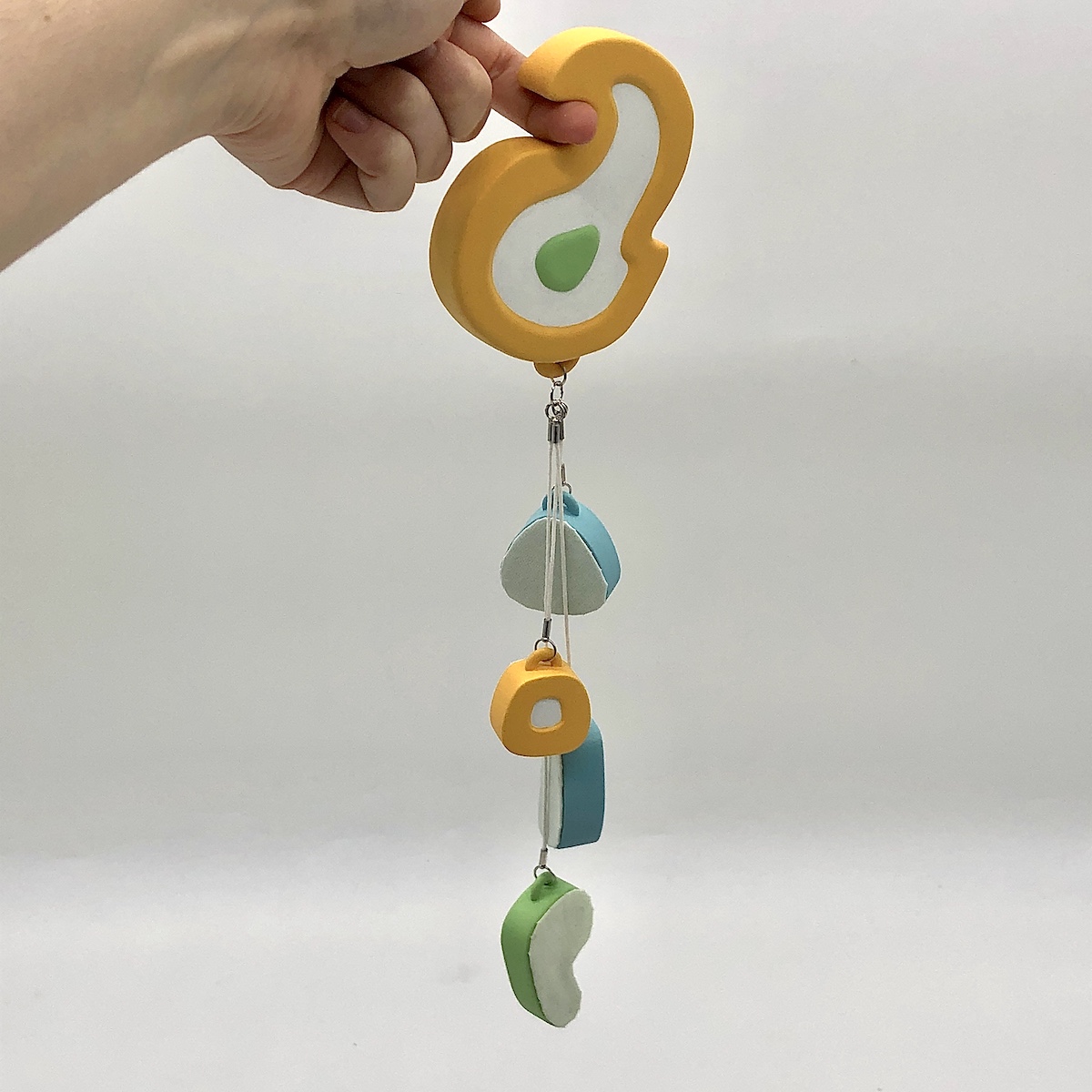 An acrylic sculpture with four smaller shapes hanging from a central point on a larger one. The colors are yellow, green, blue, and white. 