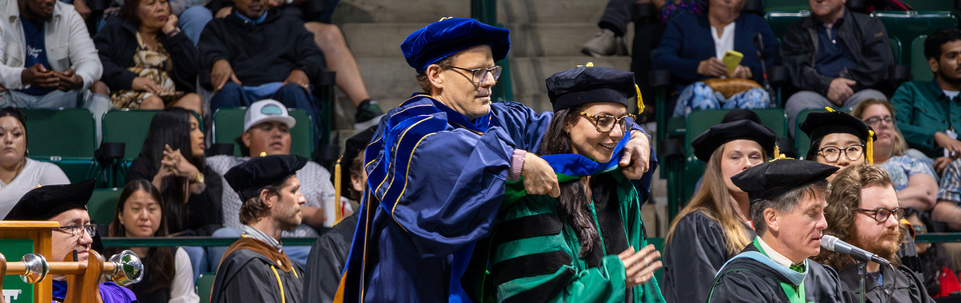 A man placing a sash over a new graduate at a commencement ceremony