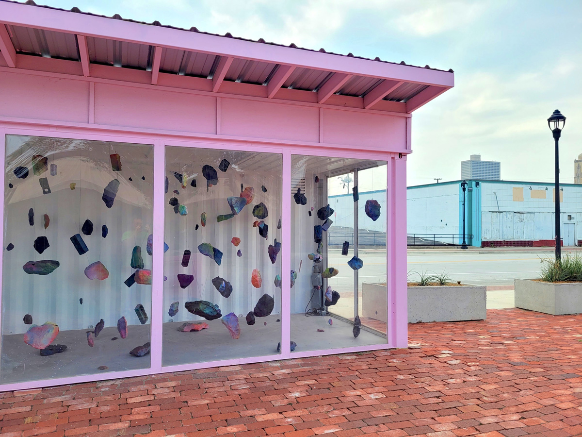 Colorfully painted plaster casts suspended from the ceiling installed outside in a pink shipping container.