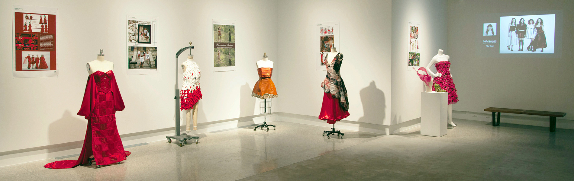 Five dresses displayed on dress forms with five posters on the wall in the CVAD Gallery.
