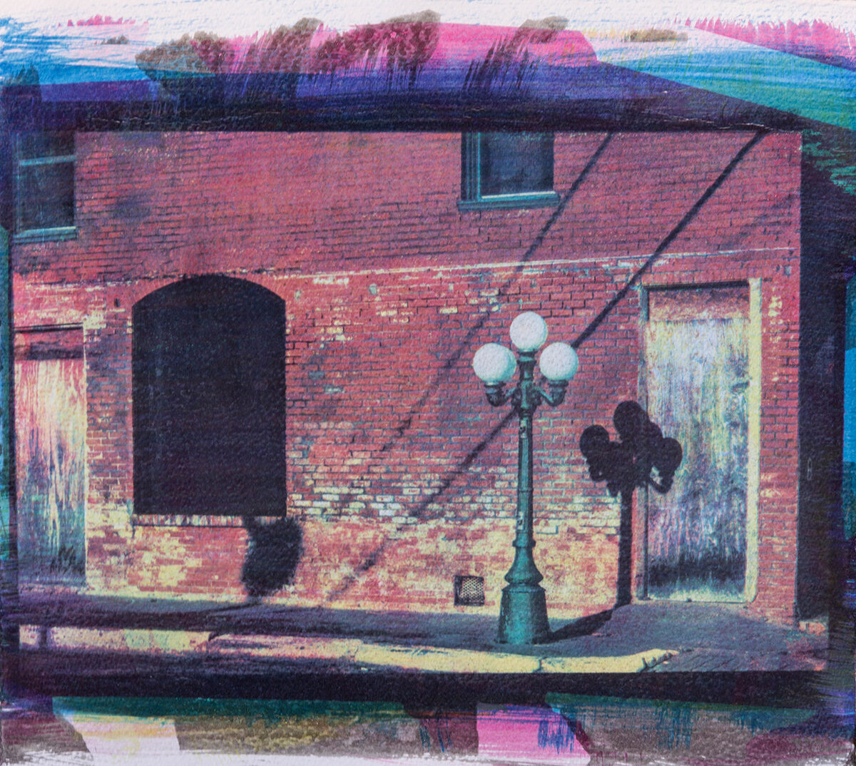 Colored photograph of a lampstand on a sidewalk in front of a brick building.