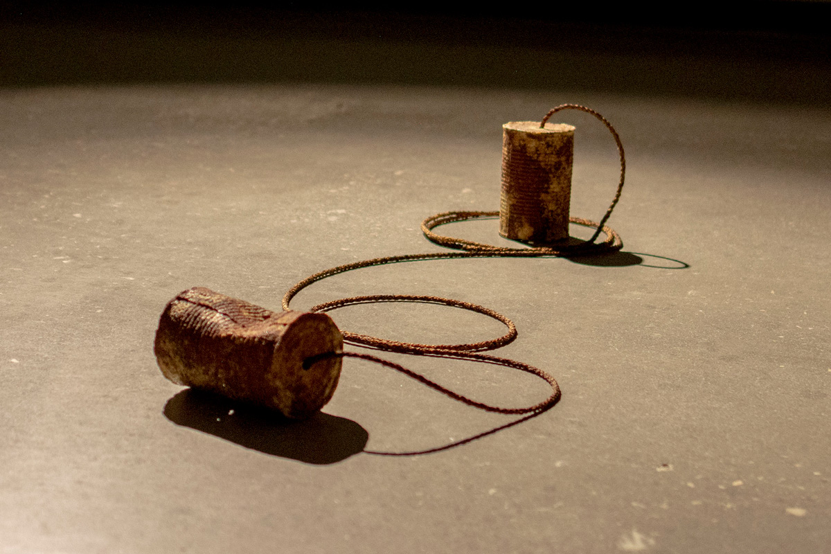 Ceramic sculpture of two tin can phones. The two phones are connected with burnt sisal rope.