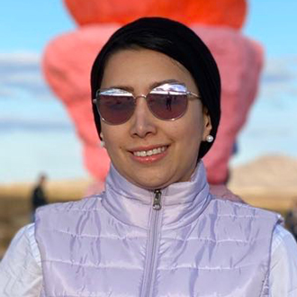 Leena facing forward smiling, wearing sunglasses, lavender-colored jacket