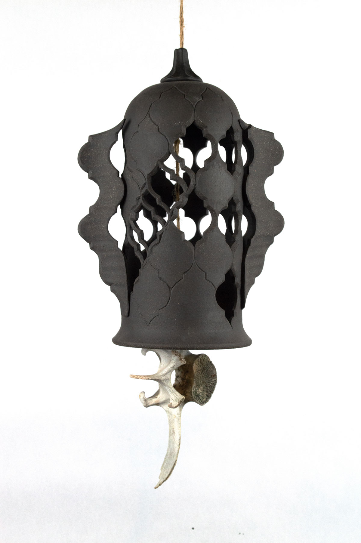 A black ceramic bell with carved and incised ornamental pattern is suspended with a cow vertebra as its clapper.