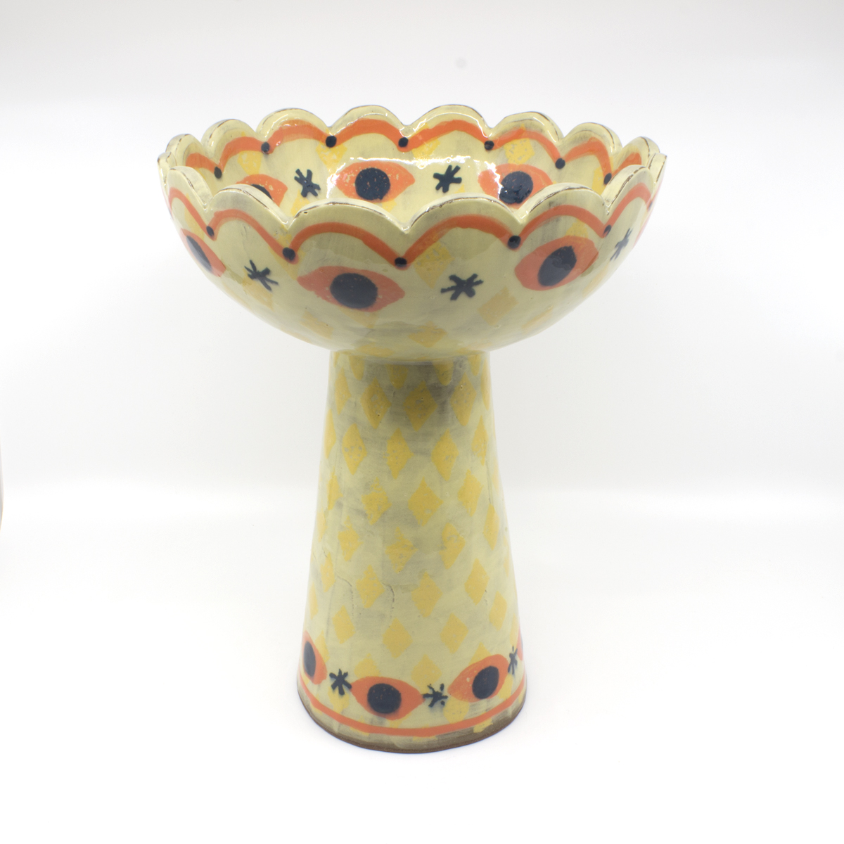 Ceramic bowl with a ceramic stand. Designed with lines, dots, stars, and eyes in yellow, navy, and orange. 