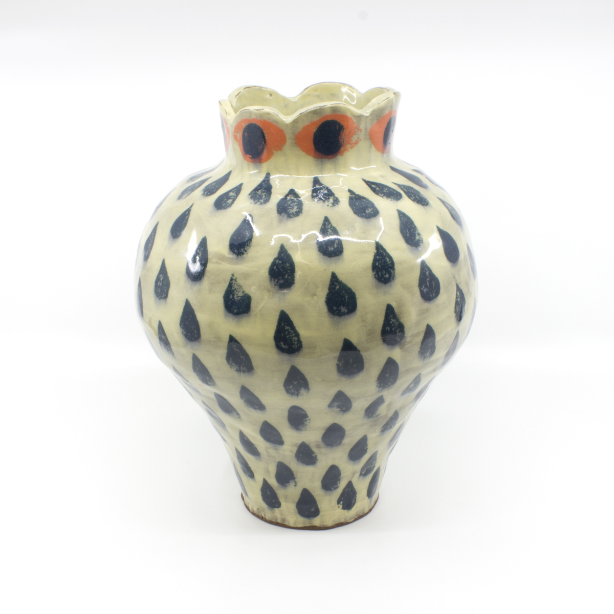 Wide ceramic vase with a narrow opening. A glazed design of navy-colored teardrops covers the vessel along with a ring of orange and navy eyes around the top.