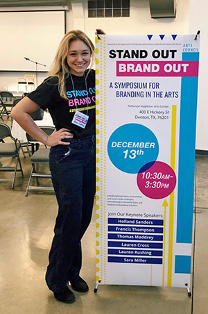 Student standing by the Stand Out Brand Out Symposium banner