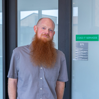 Matt Kernan leaning against the IT Services door, short hair, long red beard