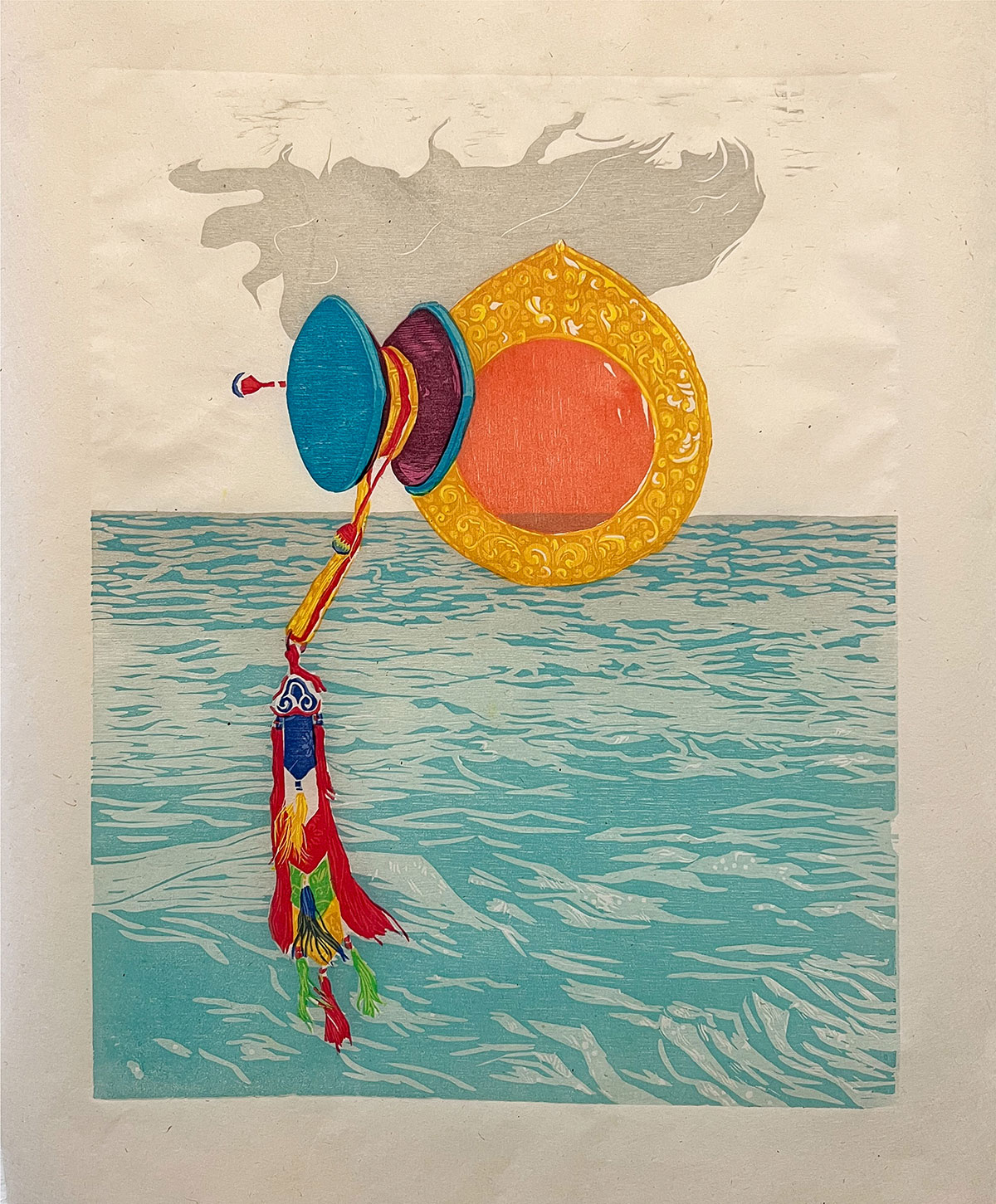 A mirror in yellow-orange and a hand drum in blue and maroon. A tassel is attached to the hand-drum. A blue body of water and a gray cloud are in the background. 