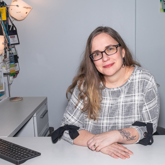 Heather Close smiling, wearing glasses, long brown hair, gray and white top