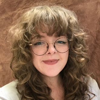 Liz smiling at the camera, head-and-shoulders, long, light brown curly hair, glasses
