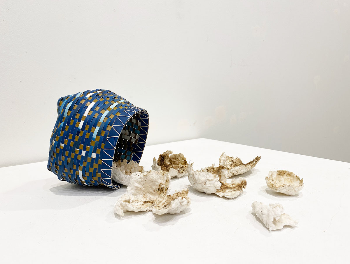 Photograph of a blue and tan woven basket laying on its side with white material coming out of it on a white table.
