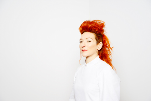 Singer and UNT alumna Shara Nova photographed from a three-quarter view from the chest up, light complected woman with long red hair wearing a white collared shirt, white background