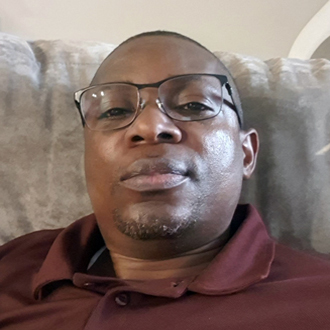 Olumuyiwa facing forward, wearing glasses, shaved head, maroon shirt