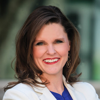 Tracey Filbeck facing forward smiling, shoulder-length hair, white jacket over a blue top.