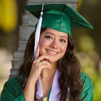 Isabel smiling, long dark hair, wearing a green cap and gown from graduation