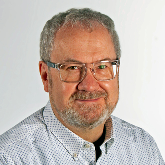 Phil Samson facing forward, smiling, short gray hair and beard, glasses, blue shirt