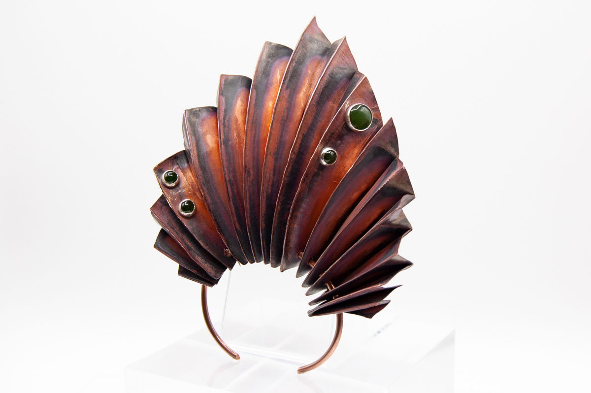 A fan-shaped cuff bracelet made from accordion folded copper with red patina, with three jade cabochons set in silver bezels.