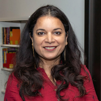 Manisha Sharma, brunette, long dark hair, smiling, wearing a necklace