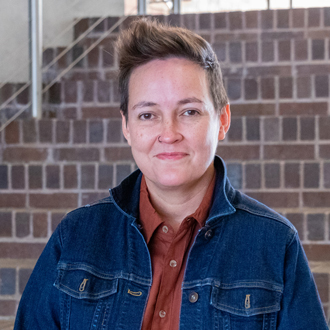 Ursula facing forward smiling with short brown hair, denim jacket and rust-colored shirt